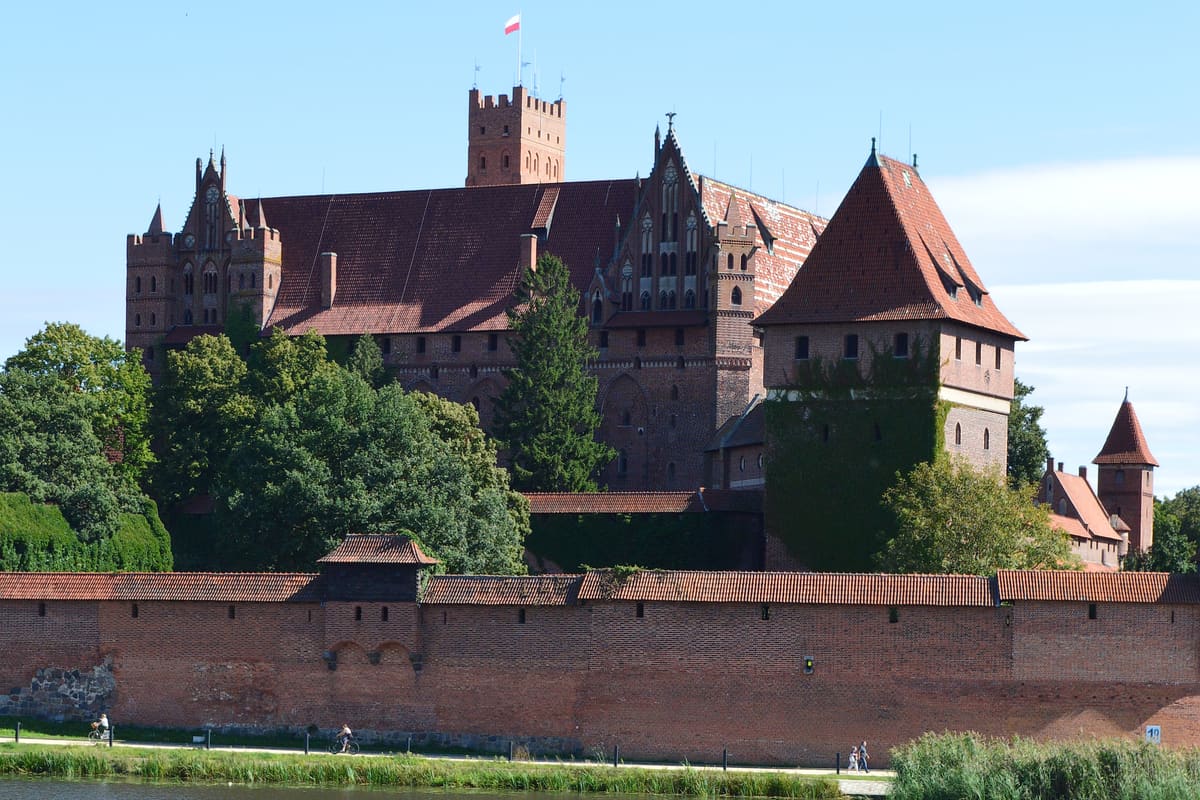 Malbork Castle (Zamek w Malborku) reflected in the Nogat river — the largest brick castle in the world, built by the Teutonic Order from 1274, reconstructed after WWII damage, UNESCO 1997.